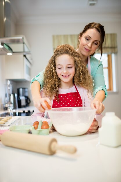 Mãe ajudando a filha em quebrar os ovos na cozinha