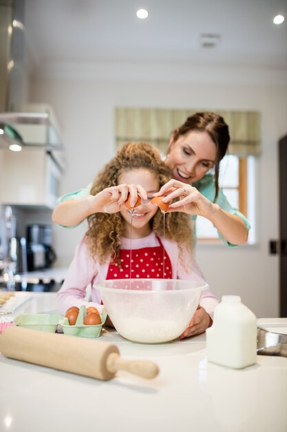 Mãe ajudando a filha em quebrar os ovos na cozinha