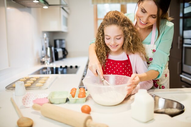 Mãe ajudando a filha no mexendo farinha na cozinha