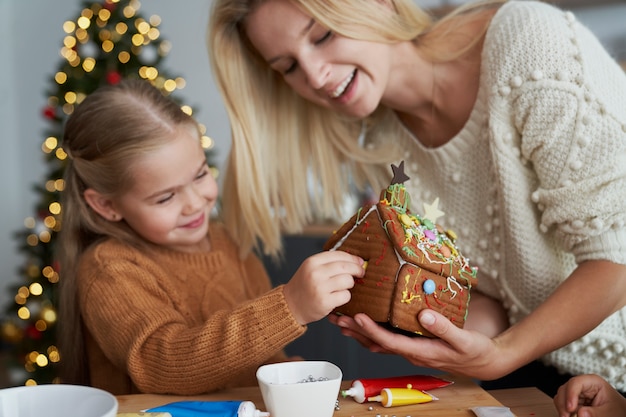 Mãe ajudando crianças a decorar uma casa de pão de gengibre