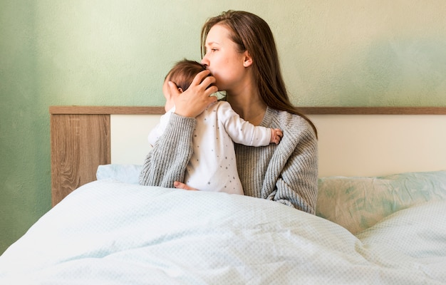 Foto grátis mãe beijando o bebê nos braços na cama