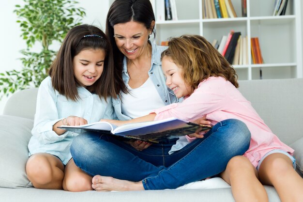Mãe bonita com suas filhas que lêem um livro em casa.