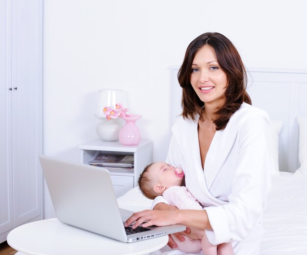 Mãe com bebê e com laptop em casa