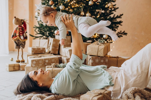 Mãe com filha deitada ao lado da árvore de natal