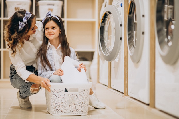 Mãe com filha lavando roupa na lavanderia self-service