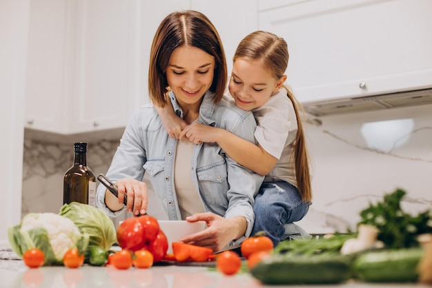 Mãe com filha preparando o jantar de legumes frescos na cozinha