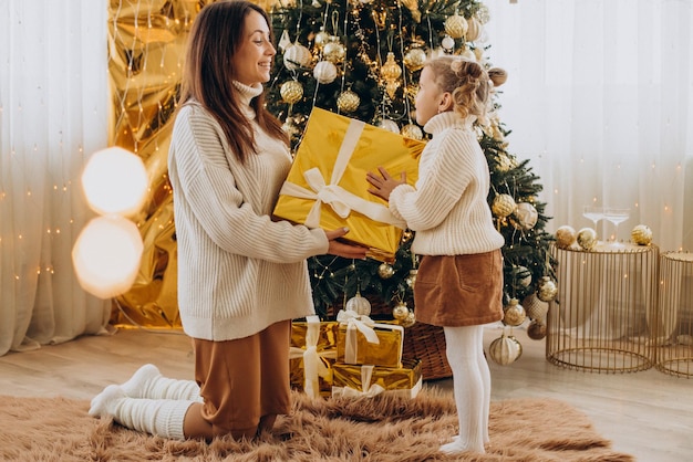 Mãe com filha segurando presente de Natal sob a árvore de Natal