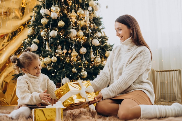 Mãe com filha segurando presente de Natal sob a árvore de Natal