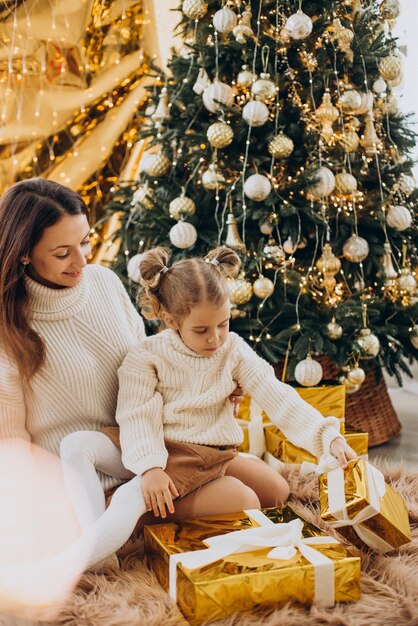 Mãe com filha segurando um presente de natal debaixo da árvore de natal