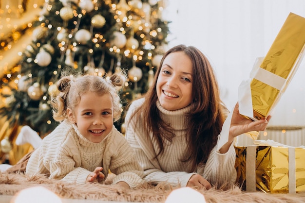 Mãe com filha segurando um presente de natal debaixo da árvore de natal