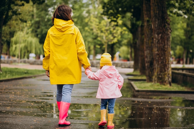 Mãe com filha vestindo capa de chuva e botas de borracha, andando em um tempo chuvoso
