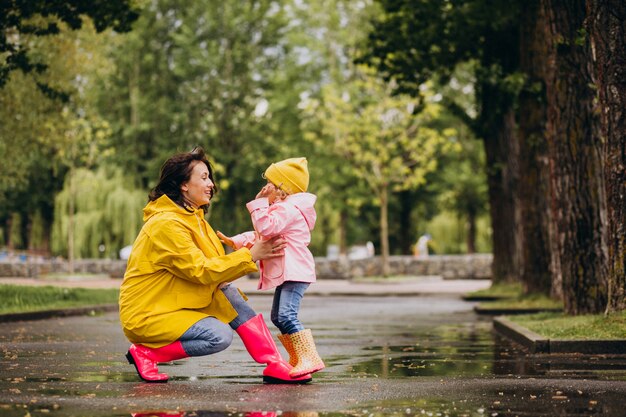 Mãe com filha vestindo capa de chuva e botas de borracha, andando em um tempo chuvoso