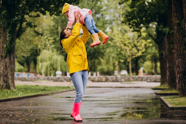 Mãe com filha vestindo capa de chuva e botas de borracha, andando em um tempo chuvoso