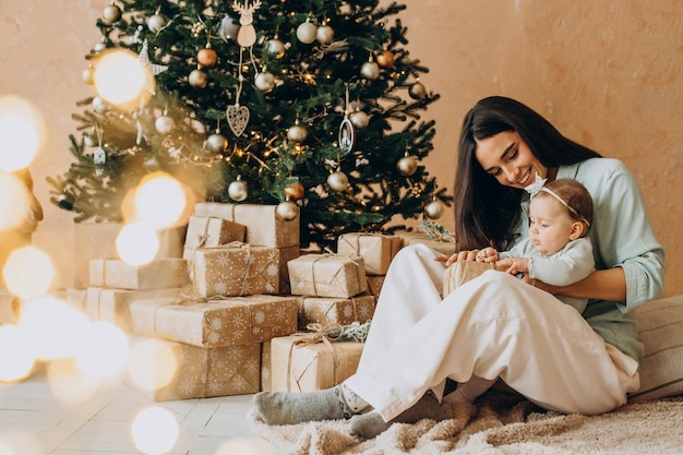 Mãe com sua filha bebê com caixas de presente perto da árvore de Natal