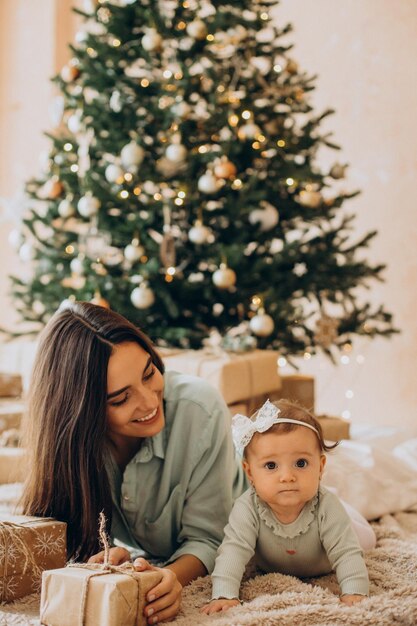 Mãe com sua filha bebê com caixas de presente perto da árvore de Natal