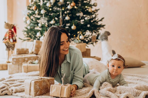 Mãe com sua filha bebê com caixas de presente perto da árvore de Natal