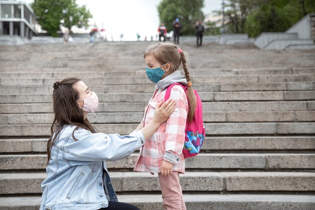 Mãe com sua filha pequena, uma colegial passando pelos degraus a caminho da escola. Conceito de educação pandêmica de Coronavirus.