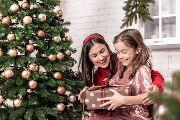 Mãe com uma filha perto da árvore de natal com uma caixa de presente