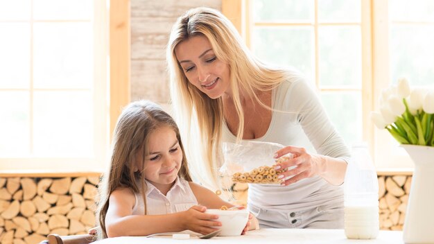 Mãe dando cereais no café da manhã para filha