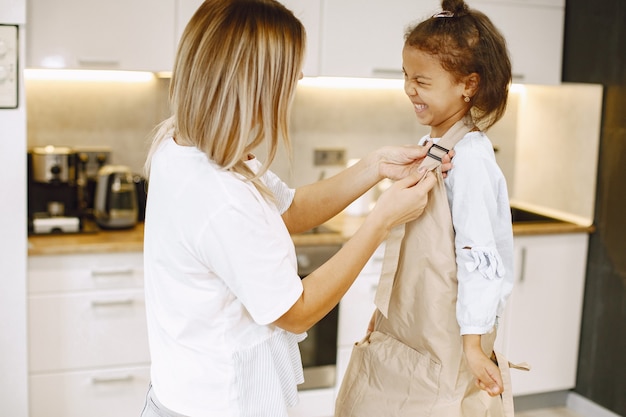 Mãe dando um avental para a filha. Mãe carinhosa e feliz cozinhando com uma criança étnica pequena