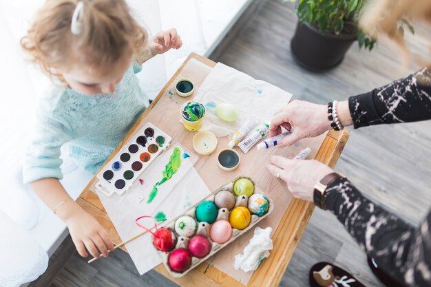 Mãe de colheita que ajuda a filha com ovos coloridos