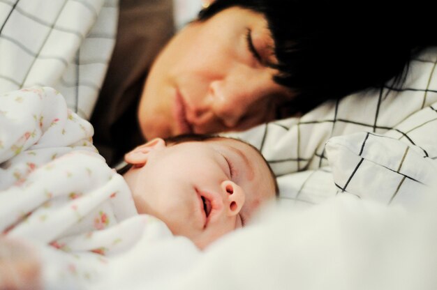 Mãe e bebê pequeno bonito que dormem junto na cama.