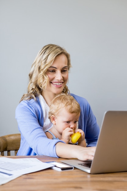 Mãe e bebê sentado à mesa e usar laptop