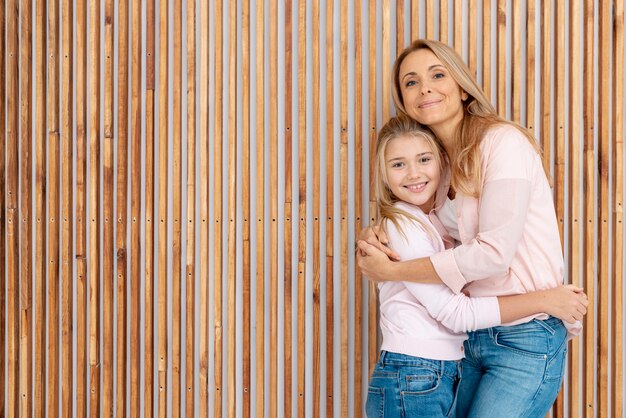 Mãe e filha abraçando ao lado de fundo de madeira