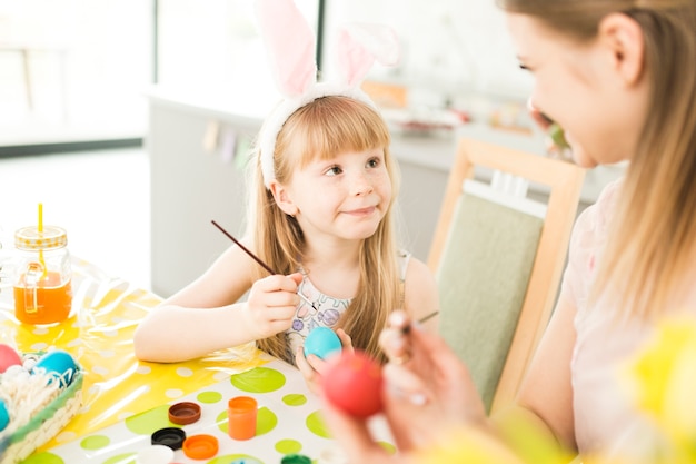 Mãe e filha alegre pintando ovos de Páscoa