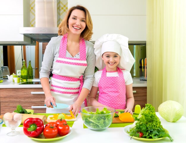 Mãe e filha alegres e sorridentes a cozinhar uma salada na cozinha