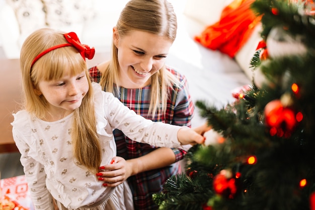 Mãe e filha alegres que decoram a árvore de Natal