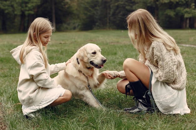 Mãe e filha brincando com o cachorro. Família no parque outono. Animal de estimação, animal doméstico e conceito de estilo de vida