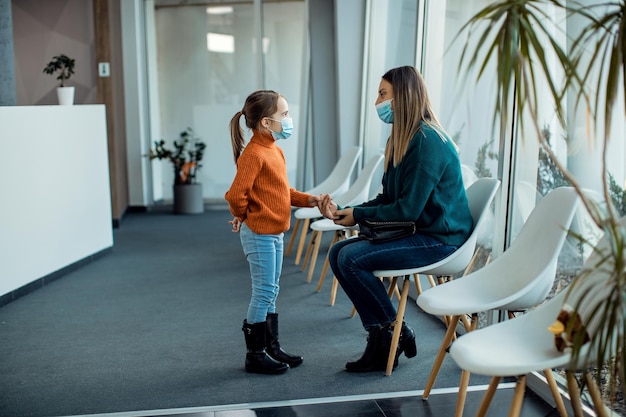 Mãe e filha com máscaras falando na sala de espera do hospital