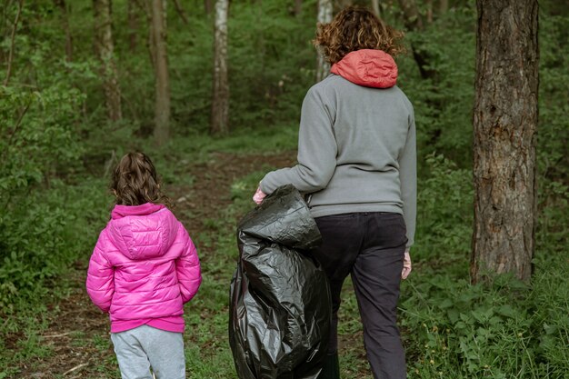 Mãe e filha com sacos de lixo limpam o meio ambiente do lixo.