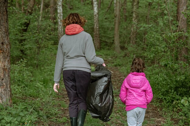 Mãe e filha com sacos de lixo limpam o meio ambiente do lixo.