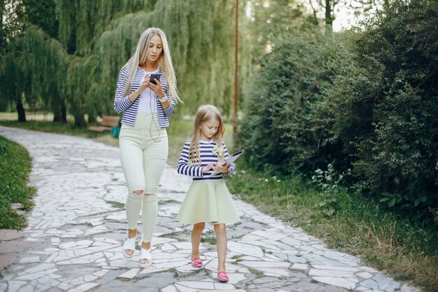 Mãe e filha com um celular e um tablet caminhando em um parque