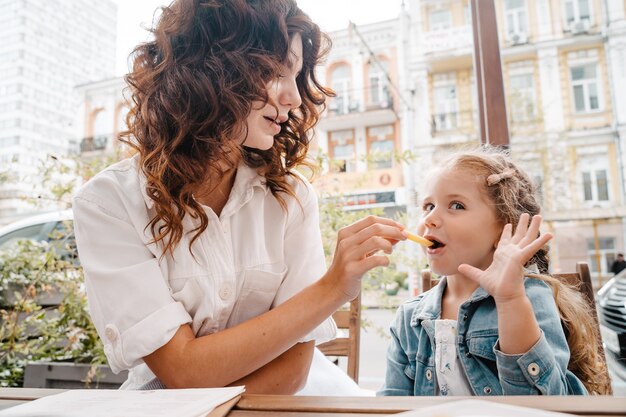 Mãe e filha comem batatas fritas em um café ao ar livre