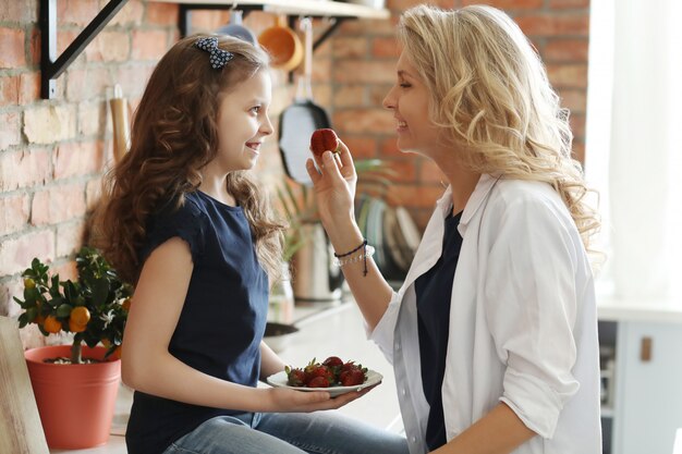 Mãe e filha comendo morangos na cozinha