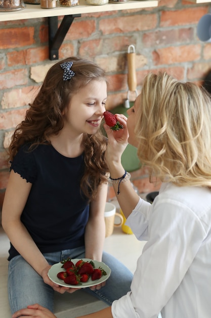 Mãe e filha comendo morangos na cozinha