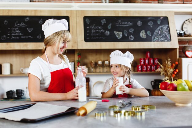 Mãe e filha encantadora se divertir bebendo leite na mesa em uma cozinha aconchegante