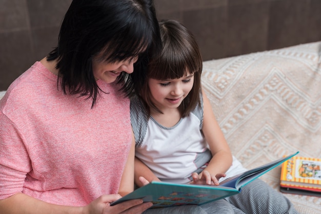 Mãe e filha lendo livro no sofá