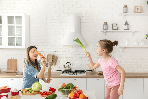 Mãe e filha preparam uma salada na cozinha. Divirta-se e brinque com legumes.