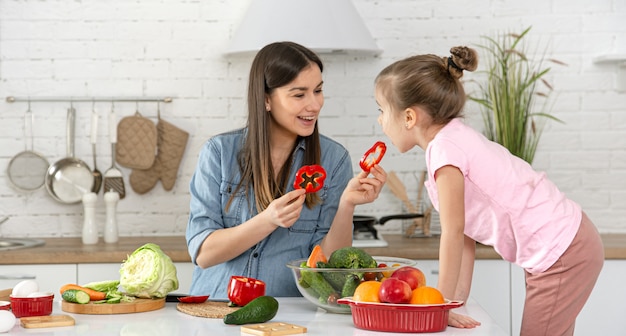 Mãe e filha preparam uma salada na cozinha. divirta-se e brinque com vegetais