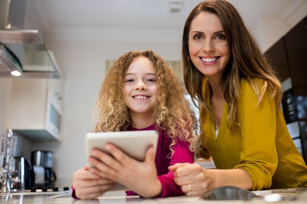 Mãe e filha que usa a tabuleta digital na cozinha