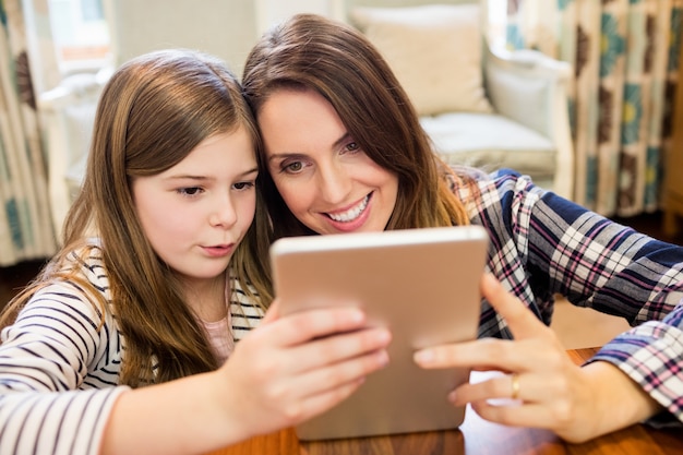 Mãe e filha que usa a tabuleta digital na sala de estar