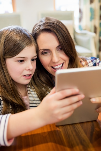 Mãe e filha que usa a tabuleta digital na sala de estar