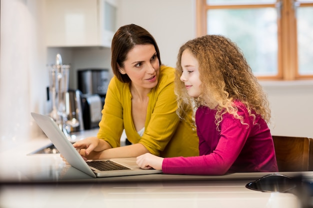 Mãe e filha que usa o portátil na cozinha