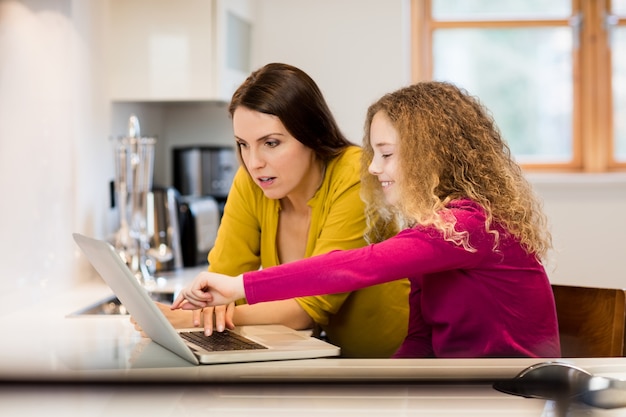 Mãe e filha que usa o portátil na cozinha