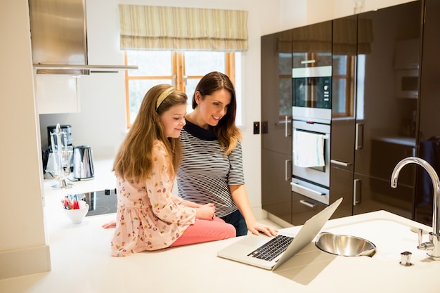 Mãe e filha que usa o portátil na cozinha