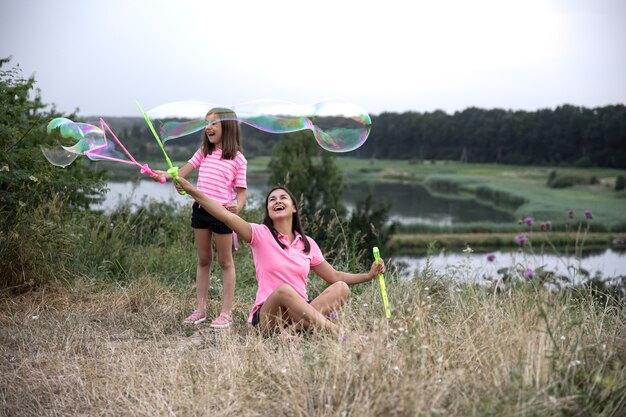 Mãe e filha se divertem juntas, fazem grandes bolhas de sabão, recreação ao ar livre.